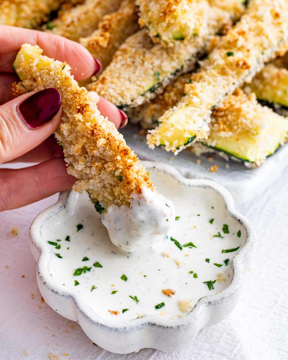 a hand dipping a zucchini stick in a little bowl with ranch dressing.