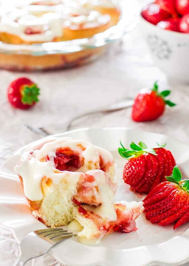 strawberry roll with cream cheese icing on a white plate with 2 strawberries on plate