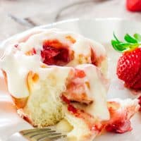a fork taking a bite of a strawberry roll on a plate