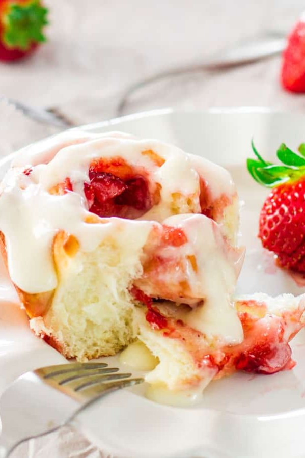 a fork taking a bite of a strawberry roll on a plate