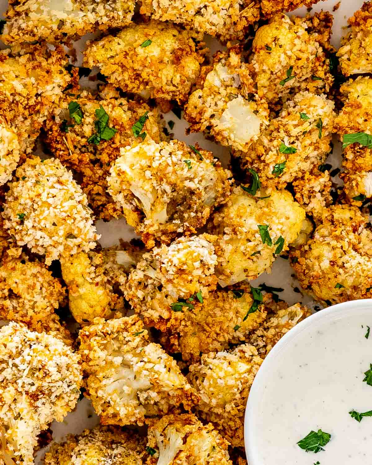 baked breaded cauliflower in a white bowl with ranch dressing.