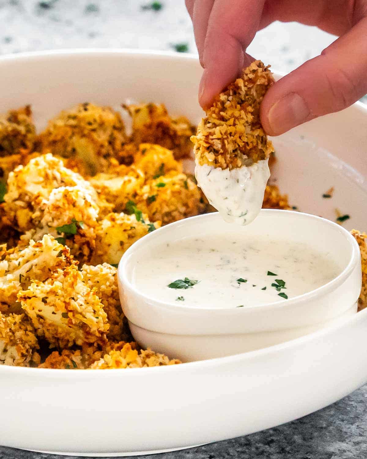 a hand dipping a breaded cauliflower piece in ranch dressing.