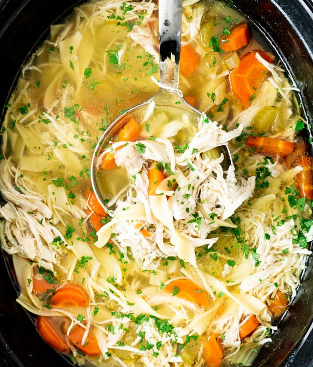 overhead shot of a ladle taking a scoop of chicken noodle soup from the crockpot