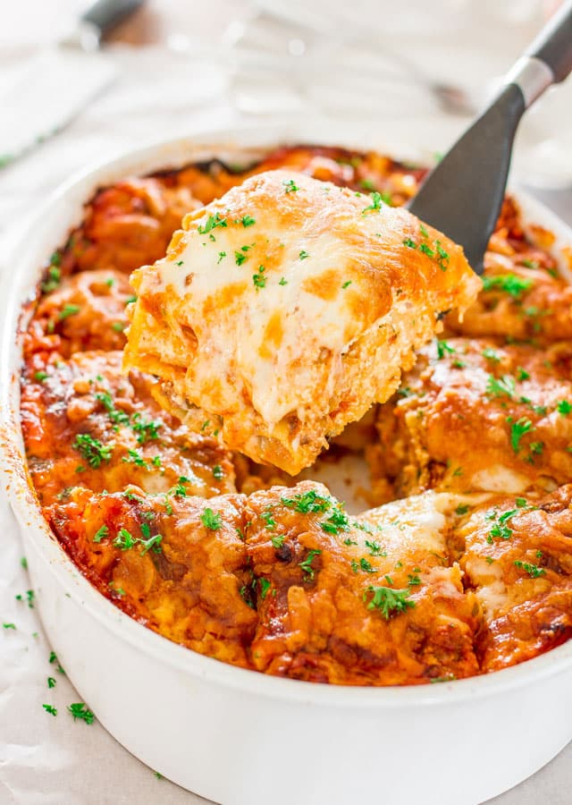 a spatula with a piece of beef lasagna held over beef lasagna in a casserole dish