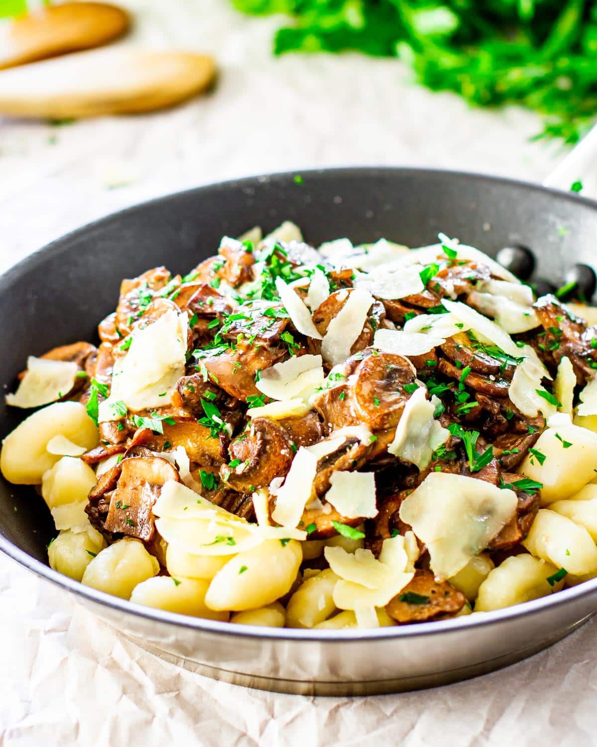 side view shot of mushroom ragu over a bed of gnocchi garnished with parmesan cheese and parsley in a skillet