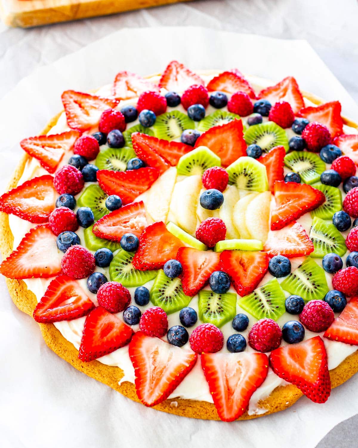 side shot of a beautiful fruit pizza on a cookie crust with cream cheese frosting