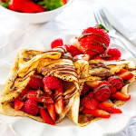 two homemade crepes stuffed with nutella and berries on a white plate