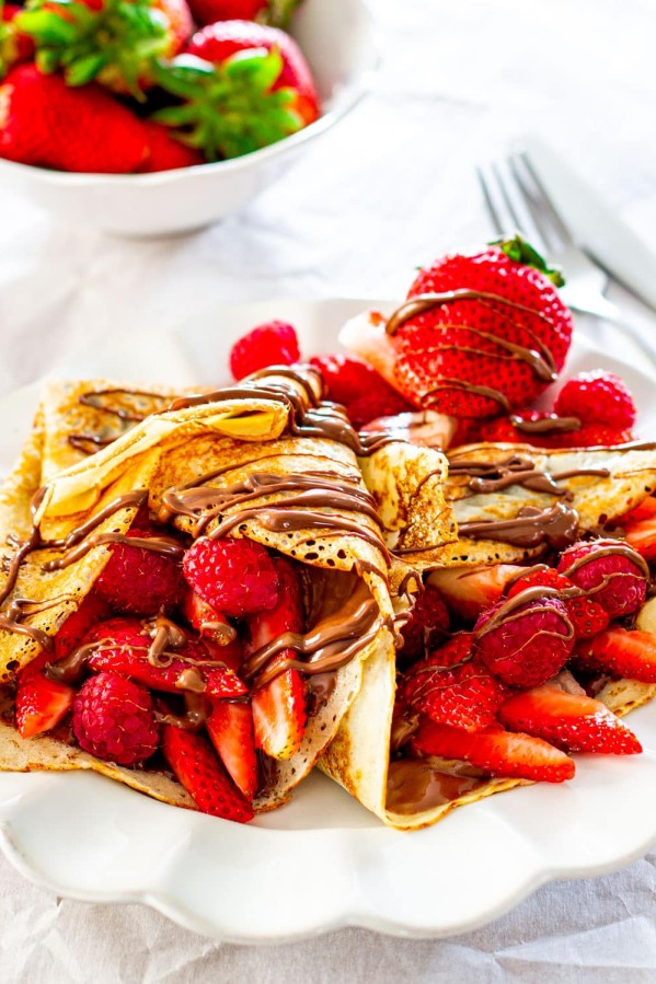 two homemade crepes stuffed with nutella and berries on a white plate