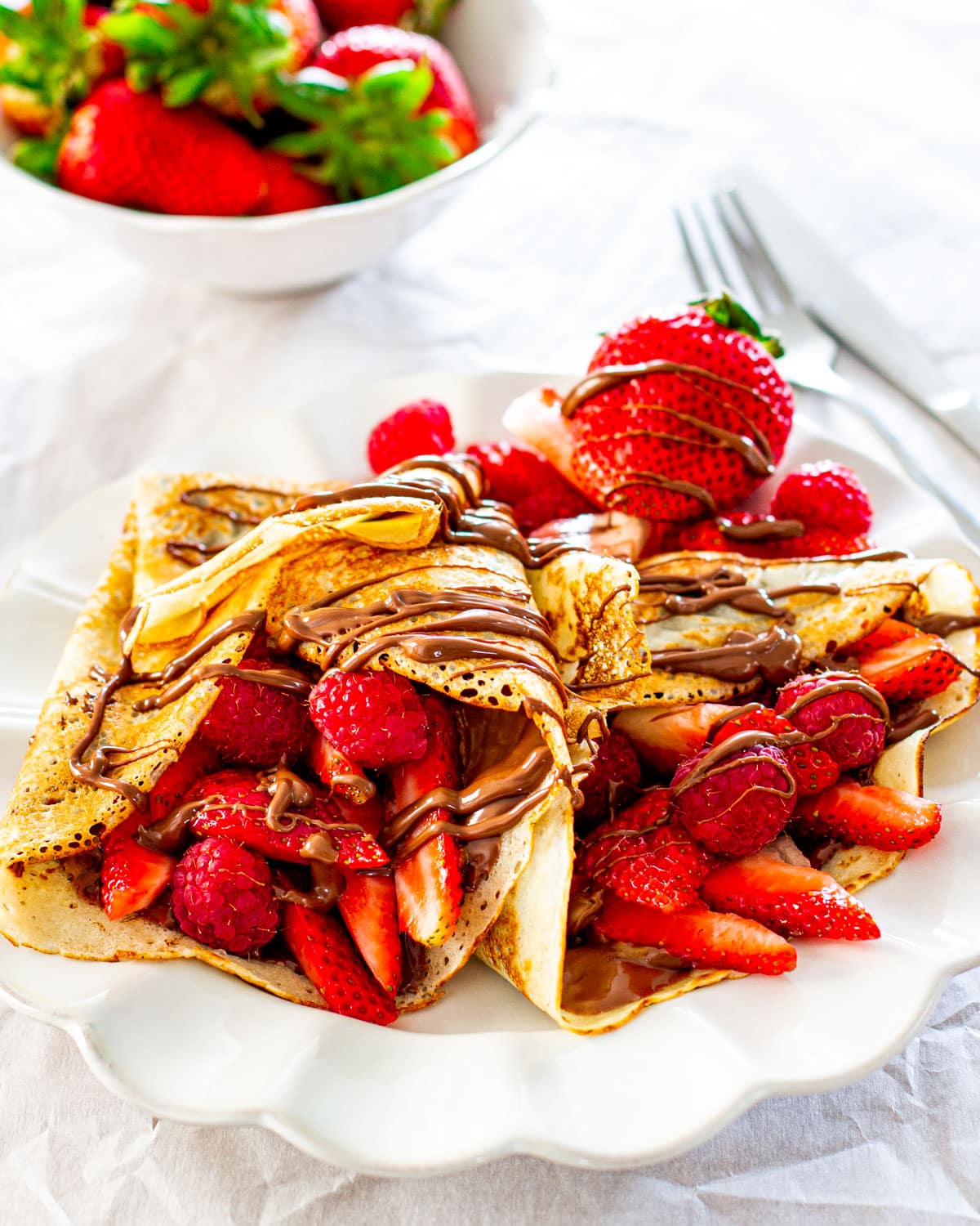 two homemade crepes stuffed with nutella and berries on a white plate