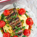 a plate with creamy polenta topped with grilled steak and roasted tomatoes