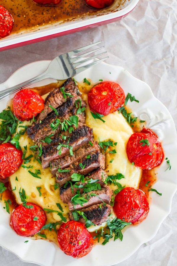 a plate with creamy polenta topped with grilled steak and roasted tomatoes