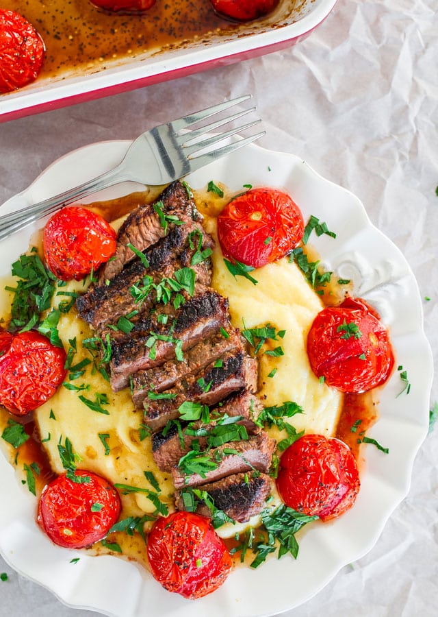 a plate with creamy polenta topped with grilled steak and roasted tomatoes