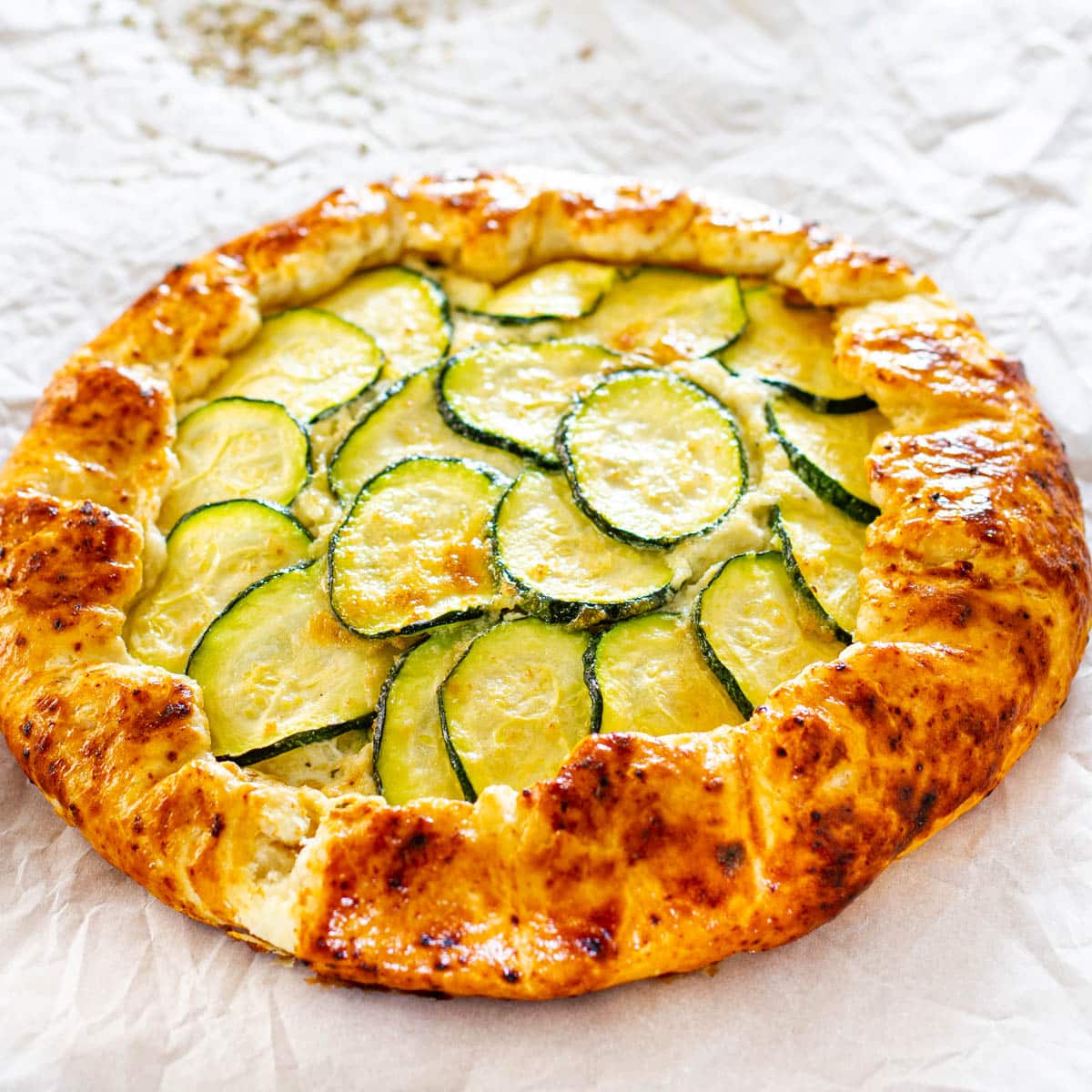 side view shot of a zucchini ricotta galette on a baking sheet lined with parchment paper fresh out of the oven