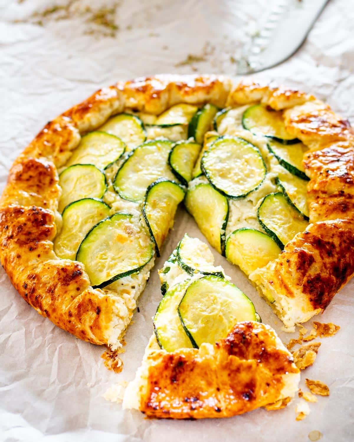 side view shot of a zucchini ricotta galette on a baking sheet lined with parchment paper fresh out of the oven with a slice cut out 