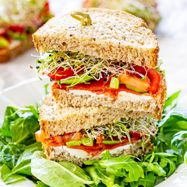 a smoked salmon loaded with veggies on whole grain bread cut in half and stacked on top of each other on a bed of arugula