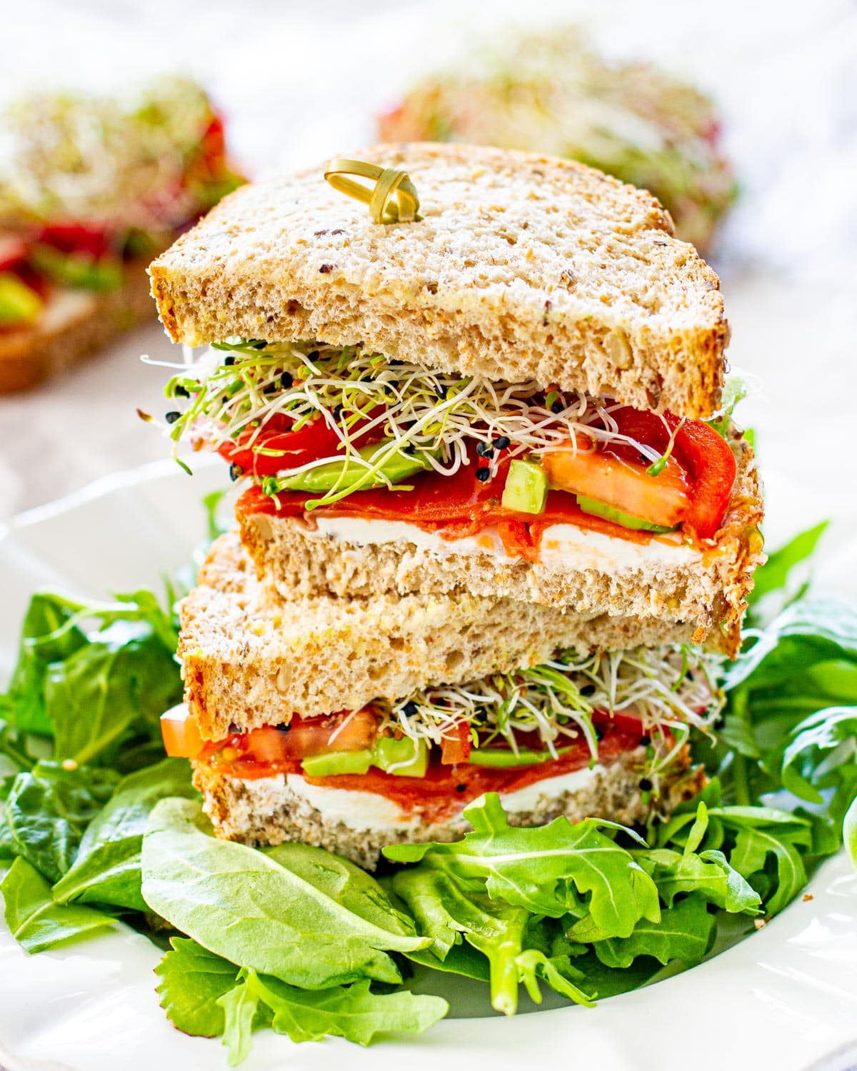 a smoked salmon loaded with veggies on whole grain bread cut in half and stacked on top of each other on a bed of arugula