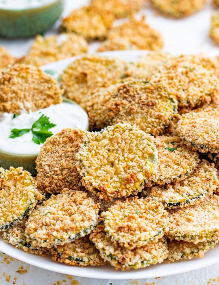 side view shot of baked zucchini crisps on a white plate with a little bowl full of ranch dressing