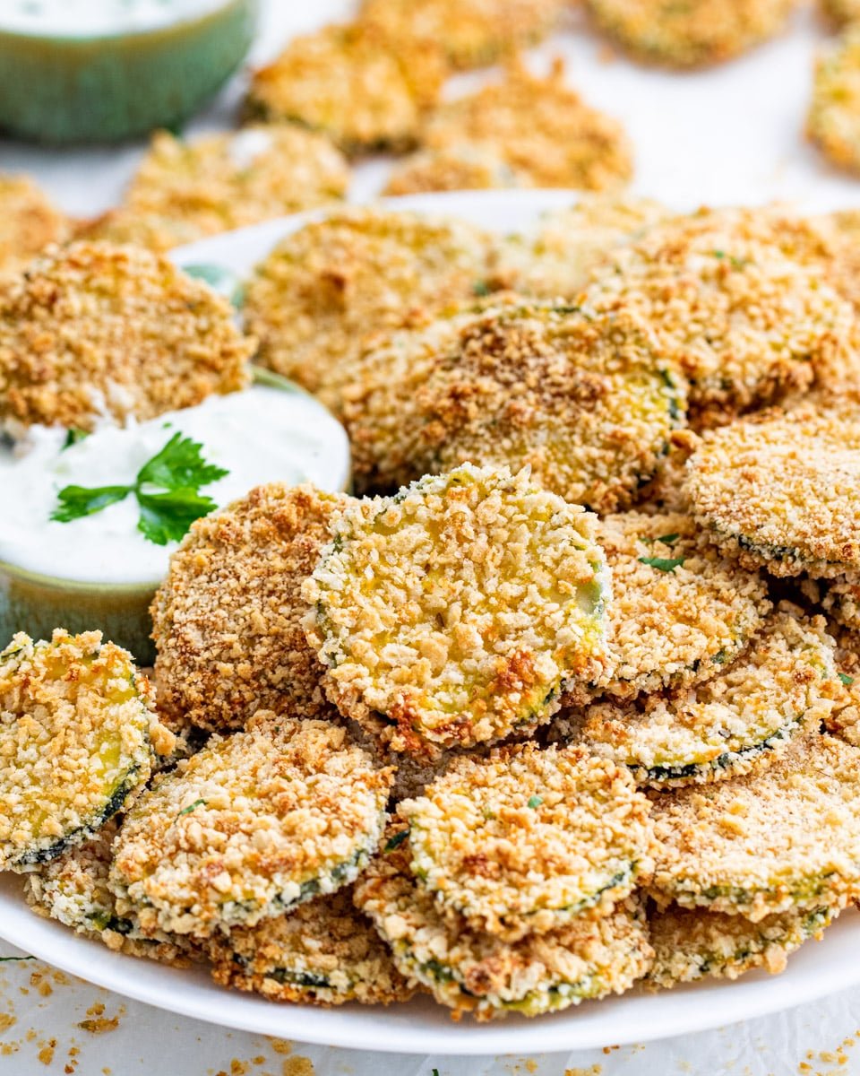 side view shot of baked zucchini crisps on a white plate with a little bowl full of ranch dressing