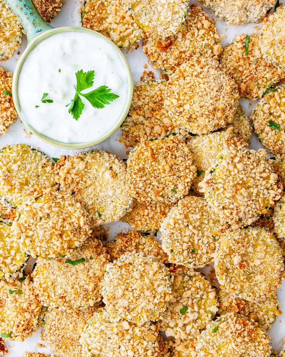 overhead shot of a bunch zucchini crisps with ranch dressing over parchment paper