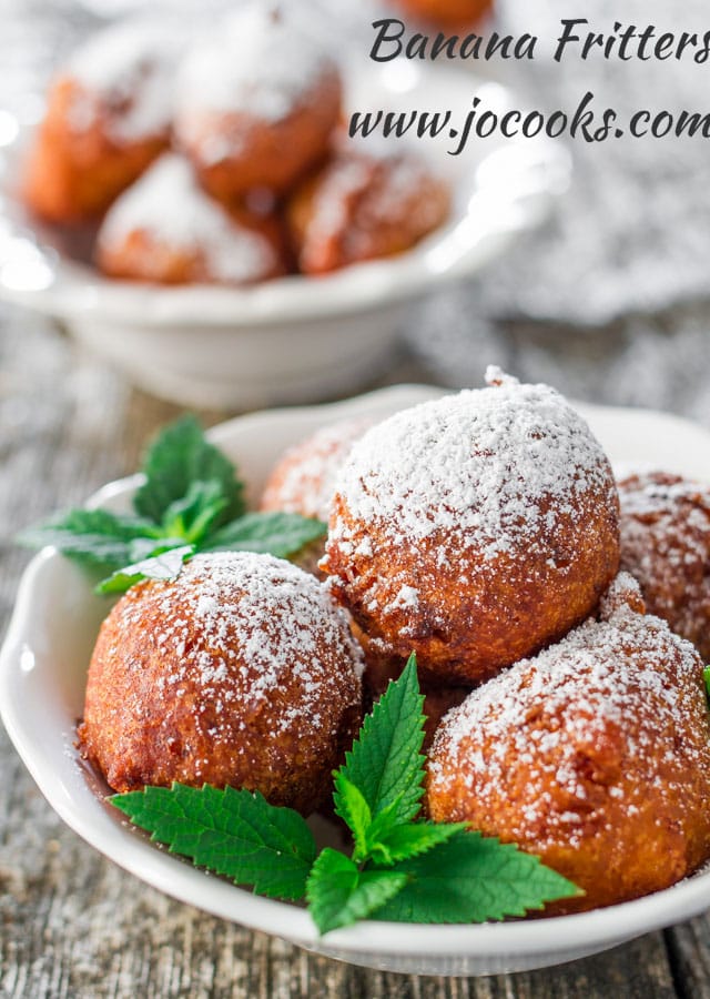 banana fritters covered in icing sugar on a white plate