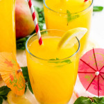 two glasses each filled with mango lemonade and a straw inside and garnished with a lemon wedge