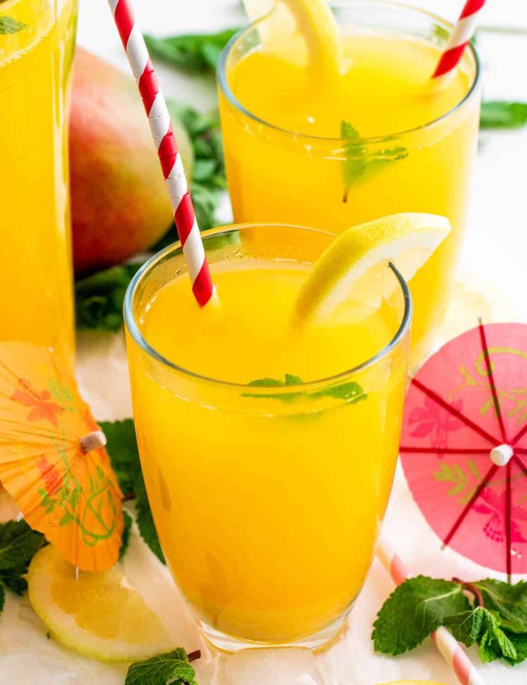 two glasses each filled with mango lemonade and a straw inside and garnished with a lemon wedge