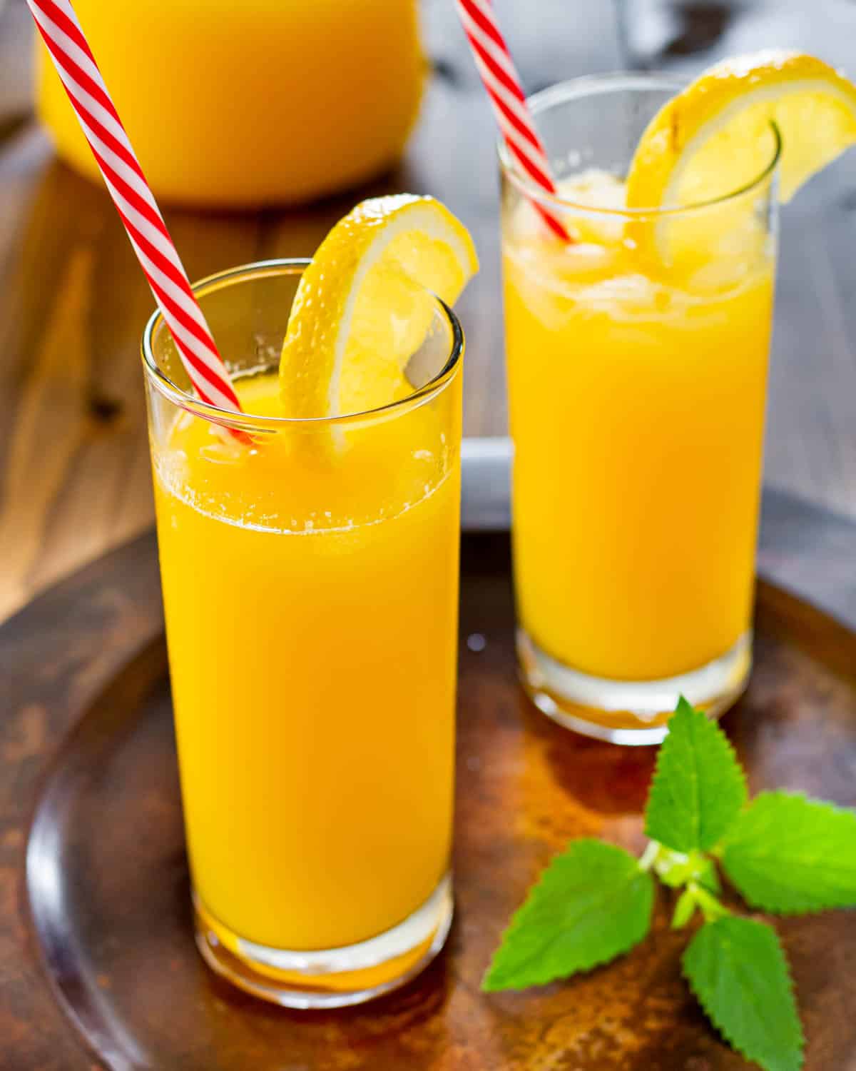 two glasses filled with mango lemonade garnished with a lemon slice and a straw in each glass