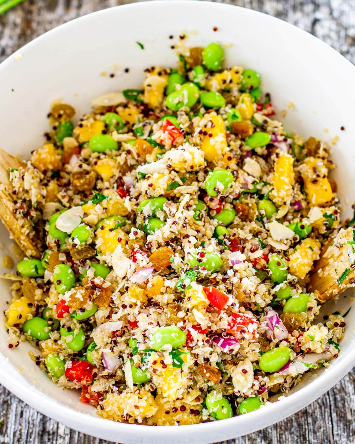 a white bowl filled with quinoa salad that's just been tossed loaded with fresh and bright ingredients