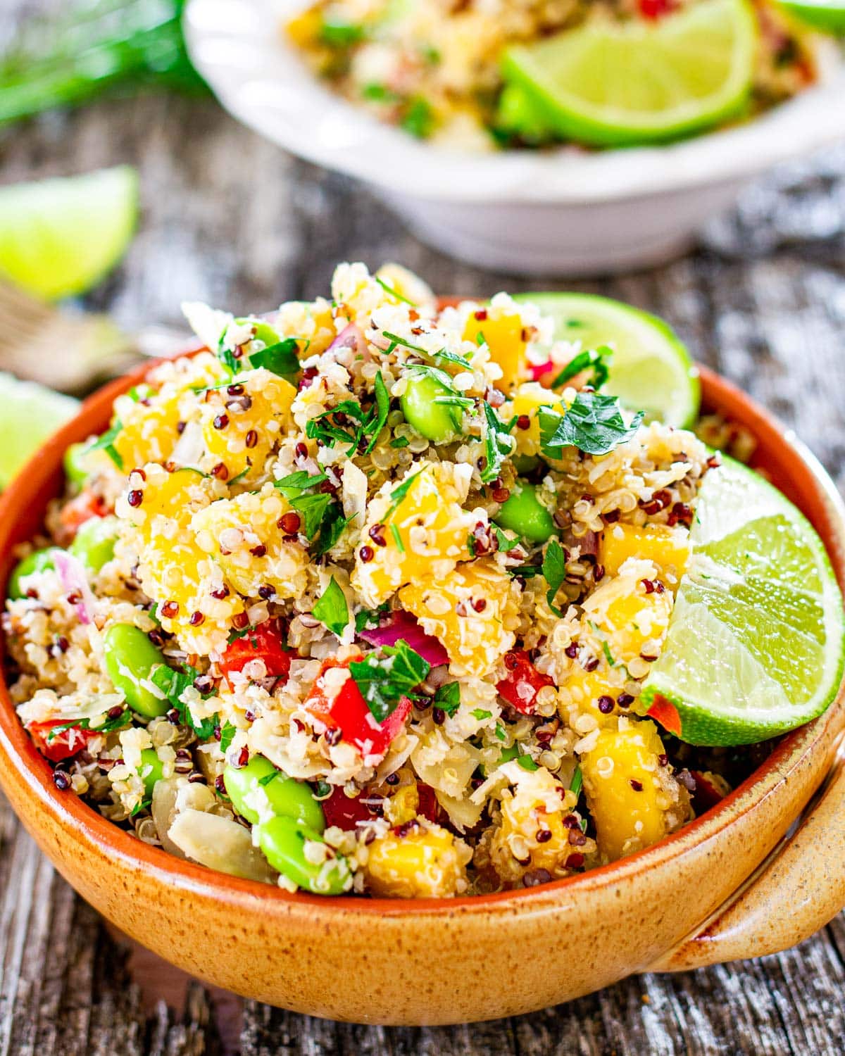 a bowl filled with a delicious quinoa salad loaded with fresh ingredients and garnished with parsley and lemon wedges