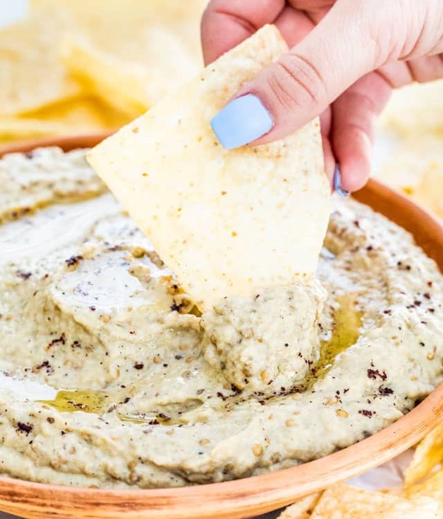 side view shot of a hand dipping a tortilla chip into the baba ganoush