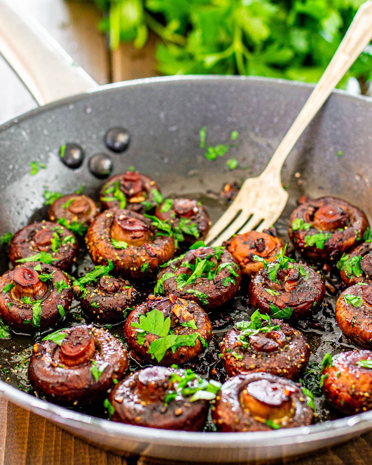 a skillet with sauteed mushrooms in red wine sauce and garnished with parsley