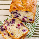 a loaf of banana blueberry bread with two slices sitting in front of it