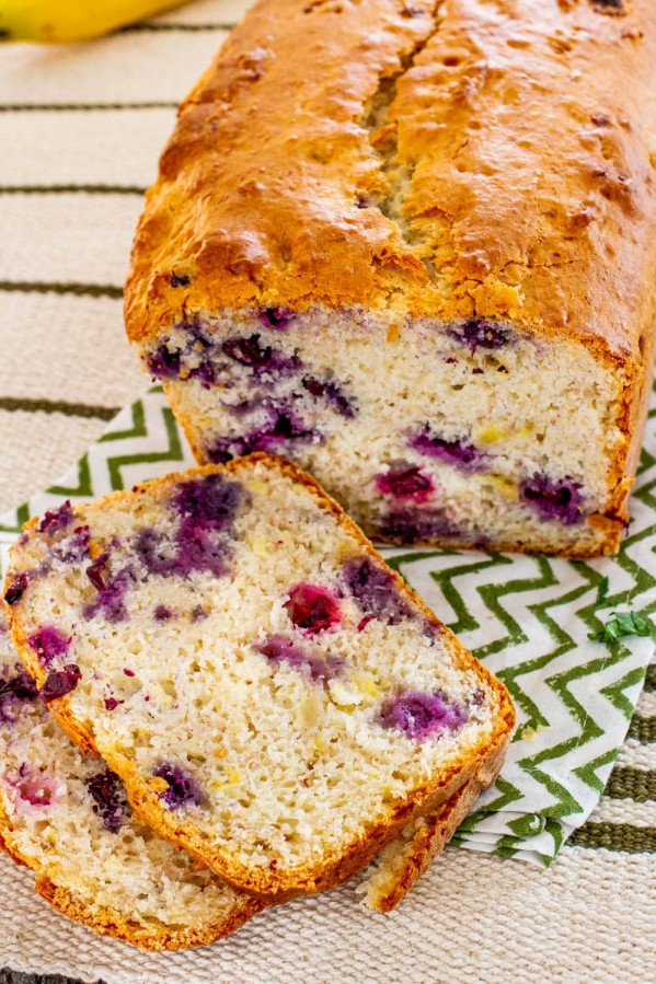 a loaf of banana blueberry bread with two slices sitting in front of it