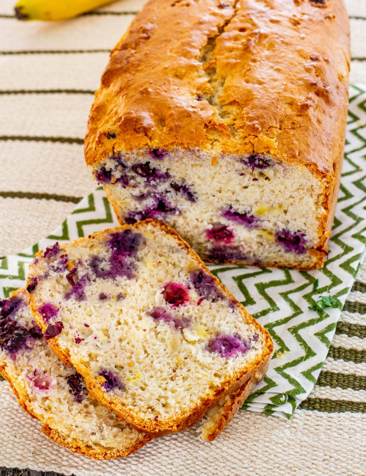 a loaf of banana blueberry bread with two slices sitting in front of it