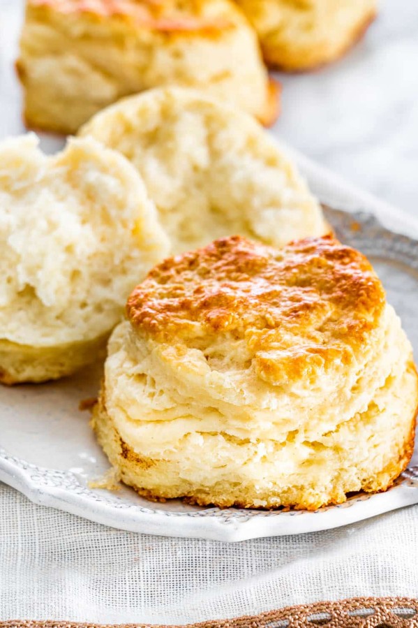 two buttermilk biscuits on a plate, one is ripped in half
