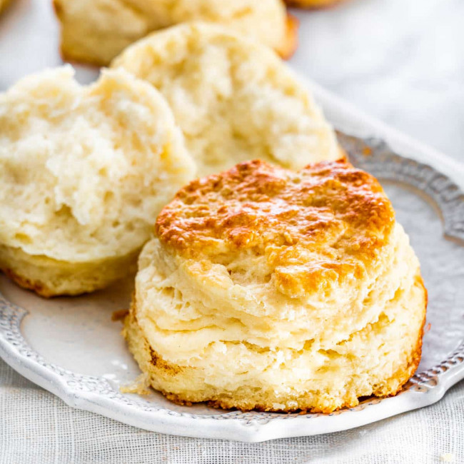 two buttermilk biscuits on a plate, one is ripped in half
