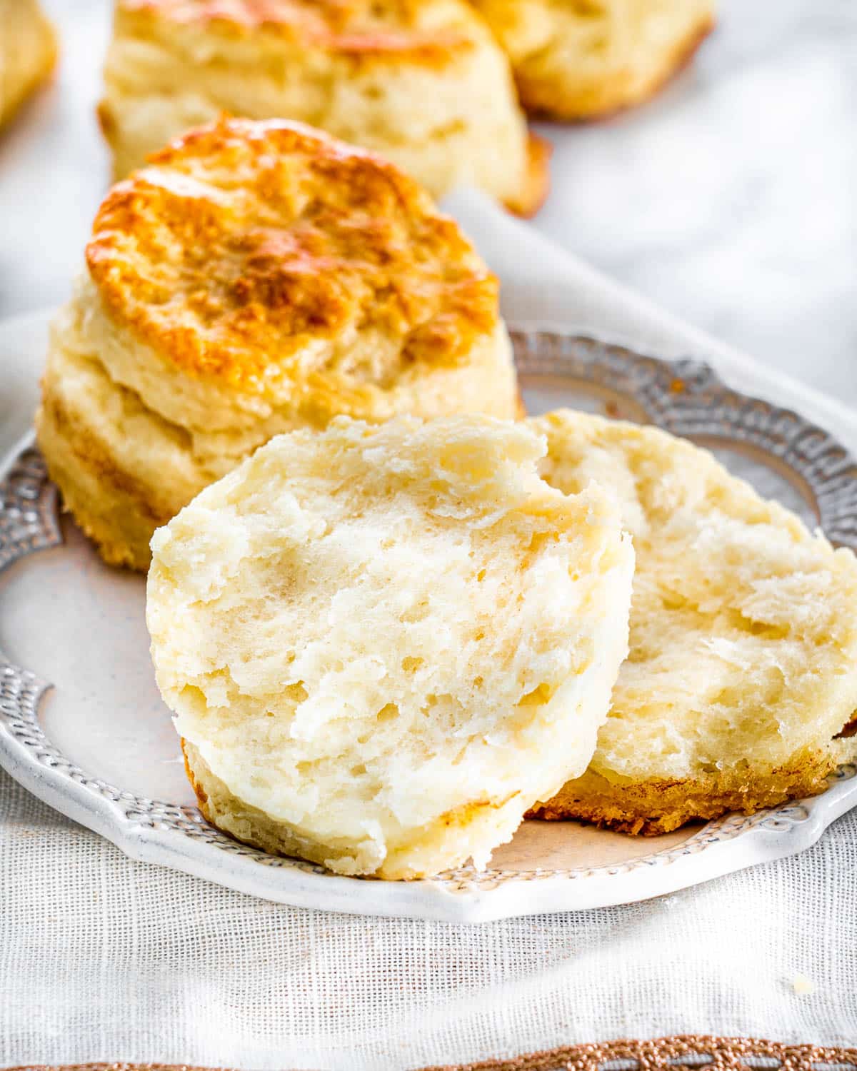 two buttermilk biscuits on a small plate with one broken in half