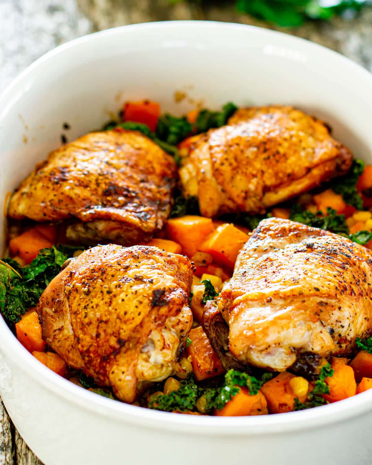 a casserole dish with 4 chicken thighs, sweet potatoes and kale fresh out of the oven