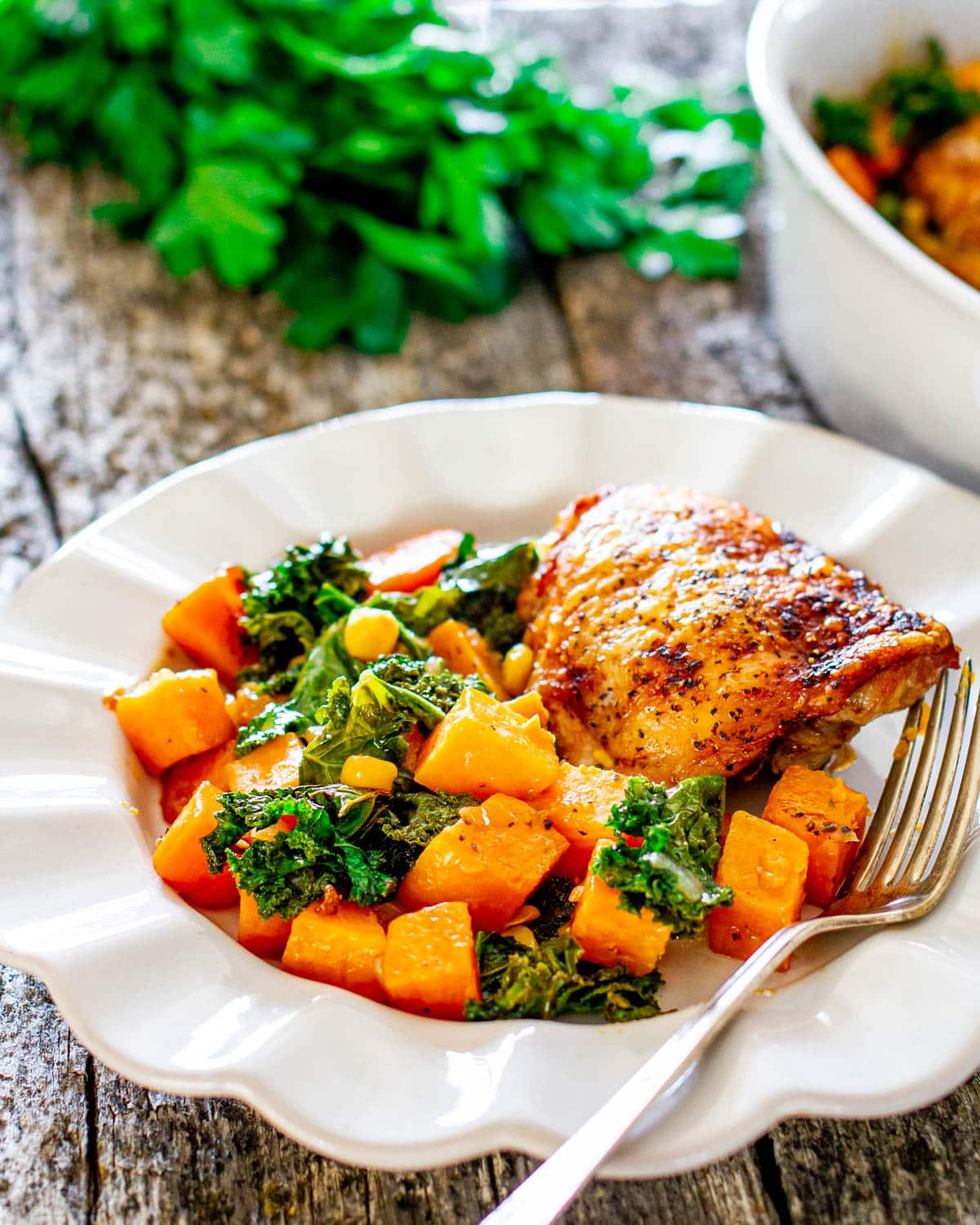 chicken thighs with sweet potatoes and kale in a white plate