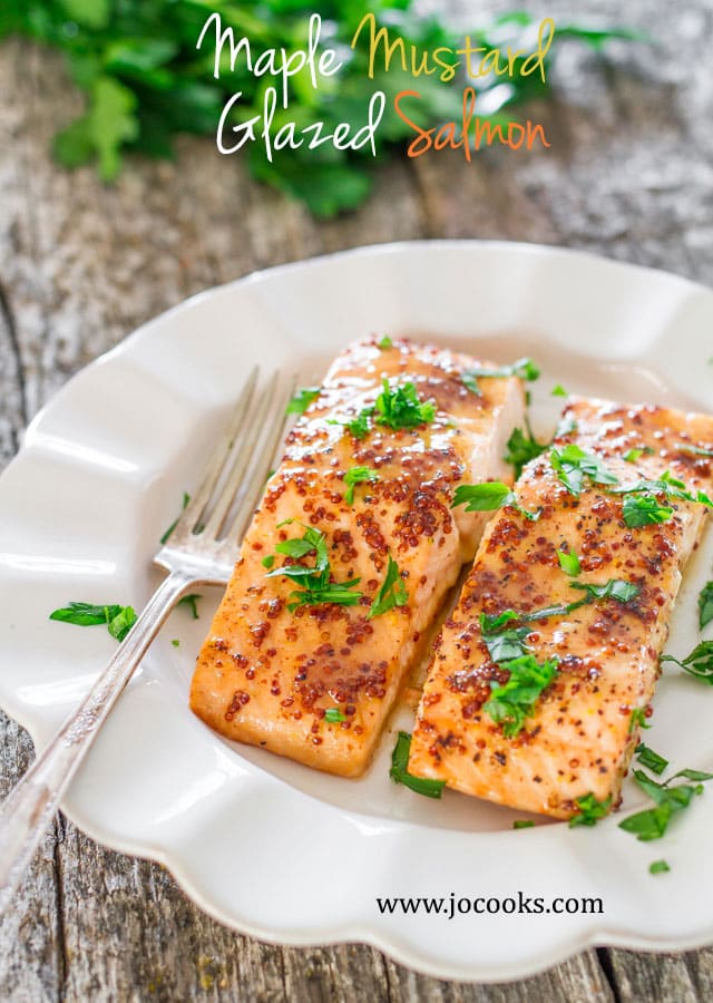 two fillets of Maple Mustard Glazed Salmon garnished with parsley on a white plate with a fork