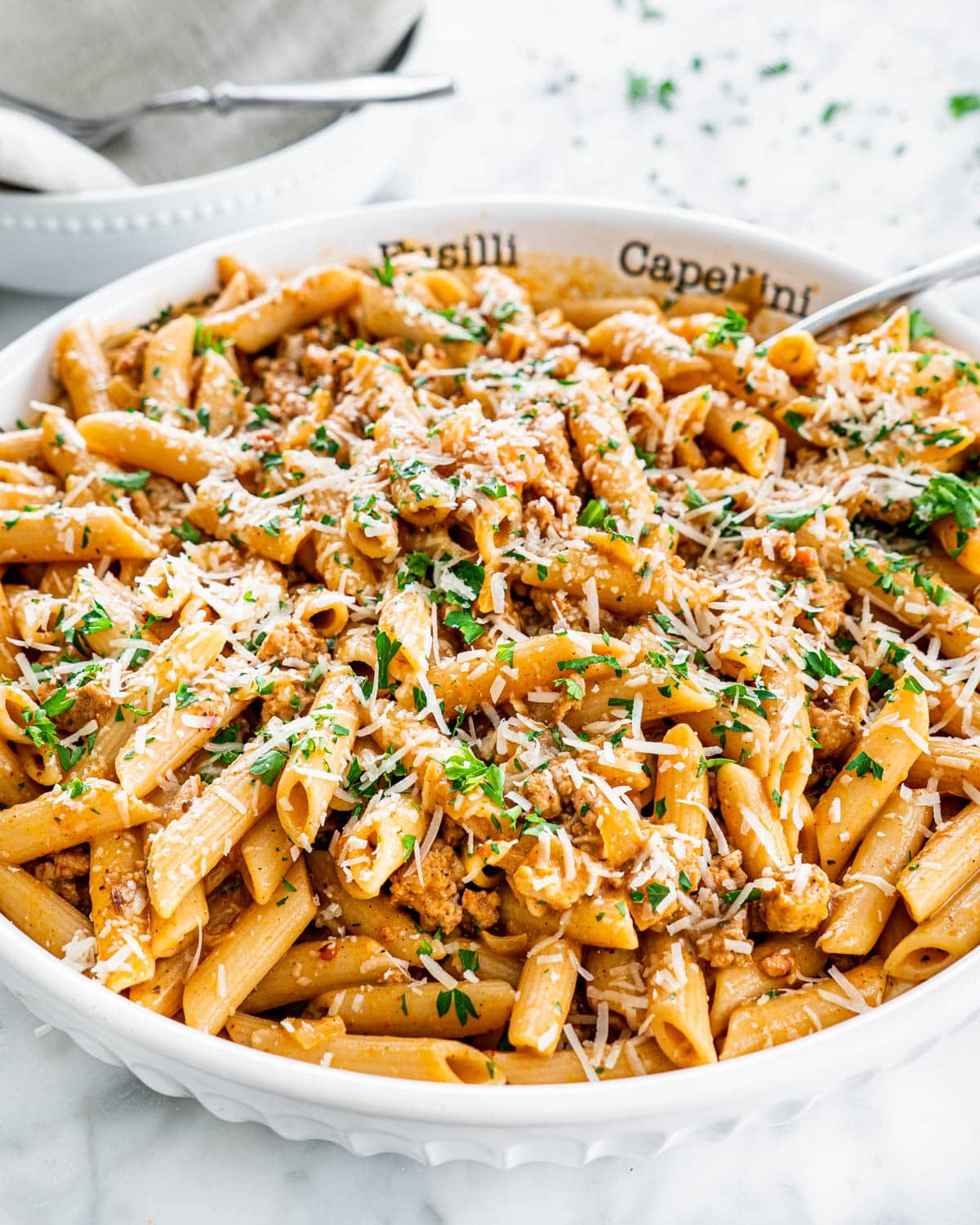 sausage pasta in a large pasta bowl garnished with parsley and parmesan cheese