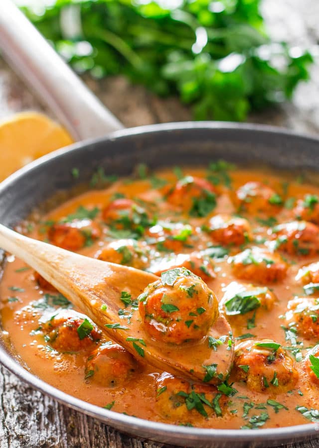 a wooden spoon scooping up a skinny thai chicken meatball from the skillet