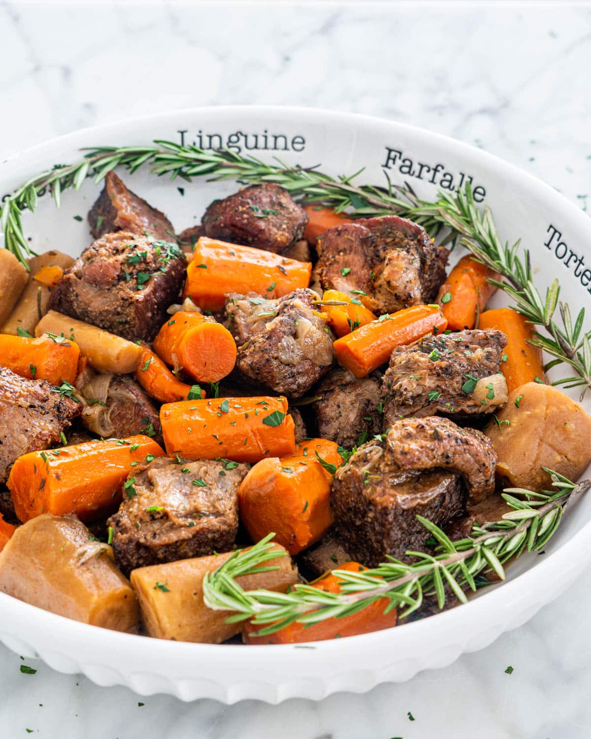 a large white bowl filled with short ribs, carrots and parsnips