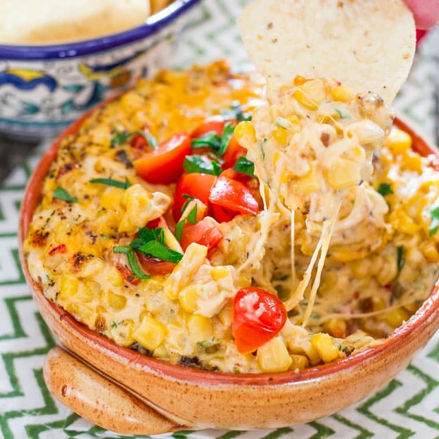 Spicy Cheesy Corn and Tomato Dip  in a bowl with a tortilla chip