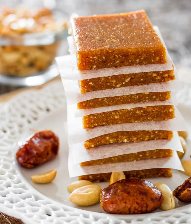 a stack of energy bars on a plate surrounded by dates and nuts