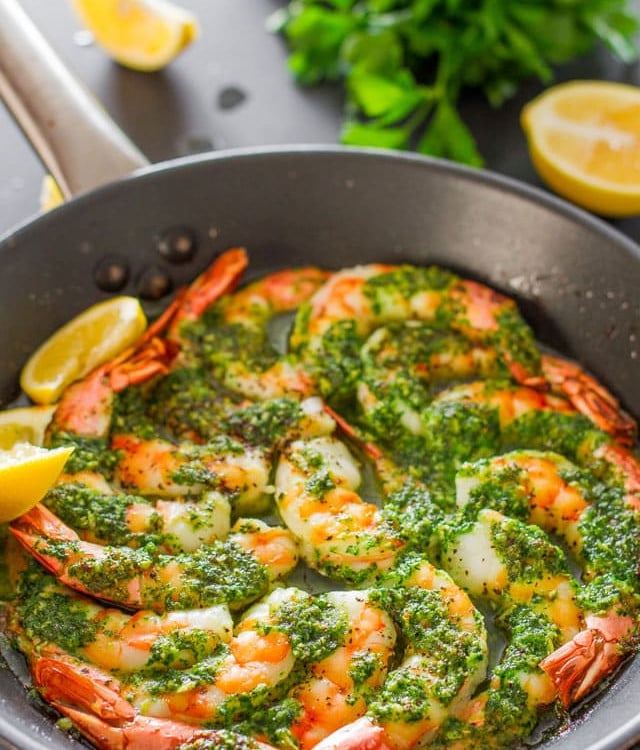 a skillet full of garlic parsley butter shrimp garnished with lemon wedges