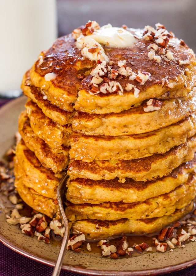 a closeup shot of a stack of pumpkin pancakes with a fork cutting down the middle