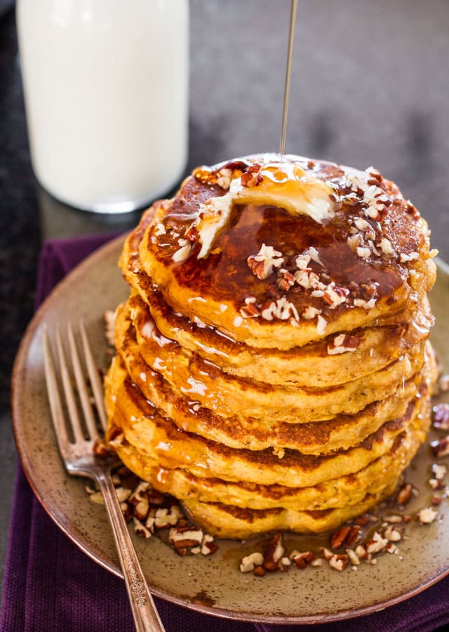 a stack of pumpkin pancakes with butter, pecans and pouring maple syrup