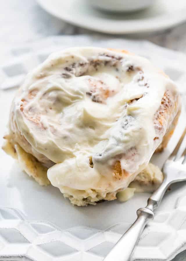 cinnabon with lots of icing on a white plate with a fork
