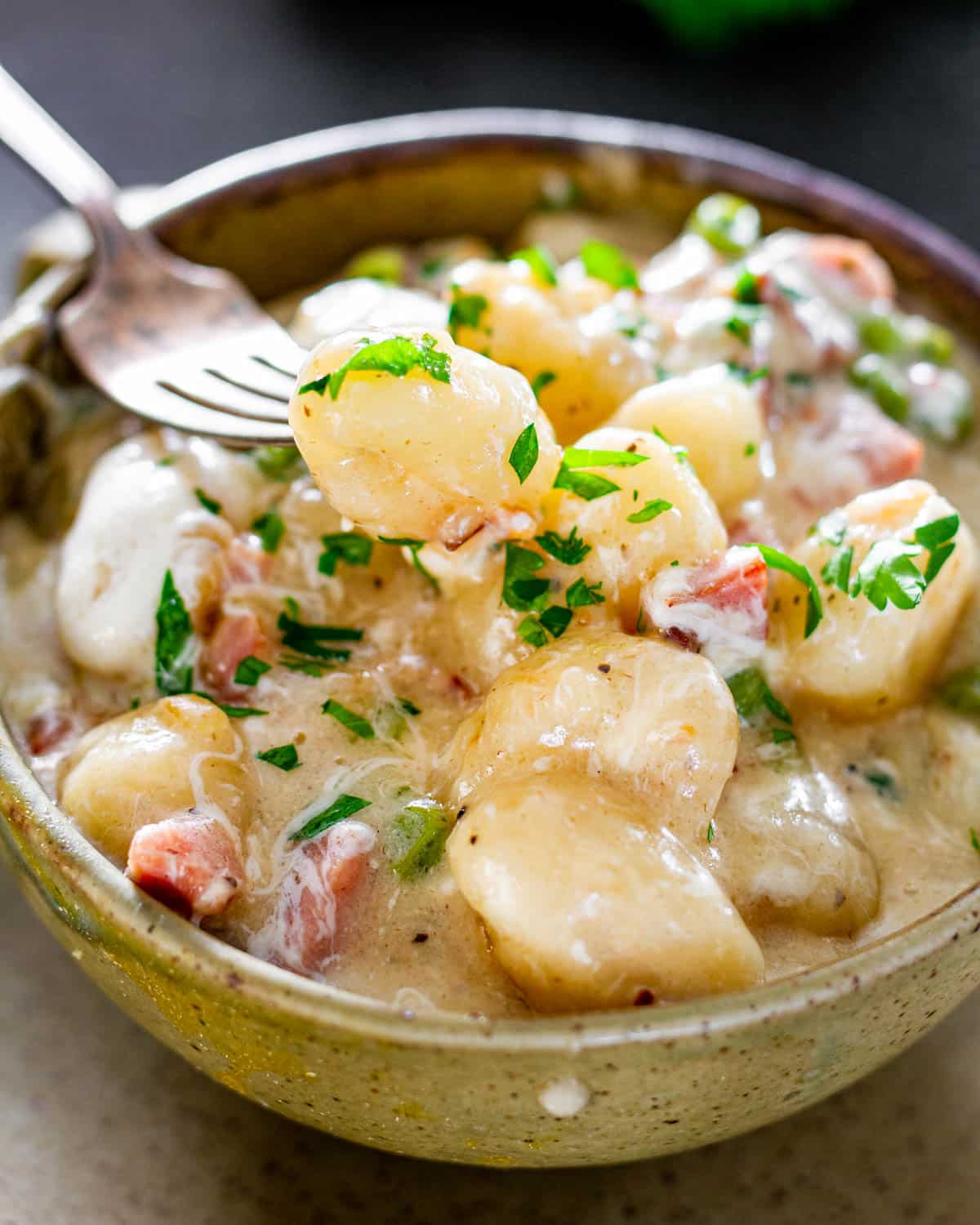 a fork holding a gnocchi above a bowl filled with creamy cheesy gnocchi